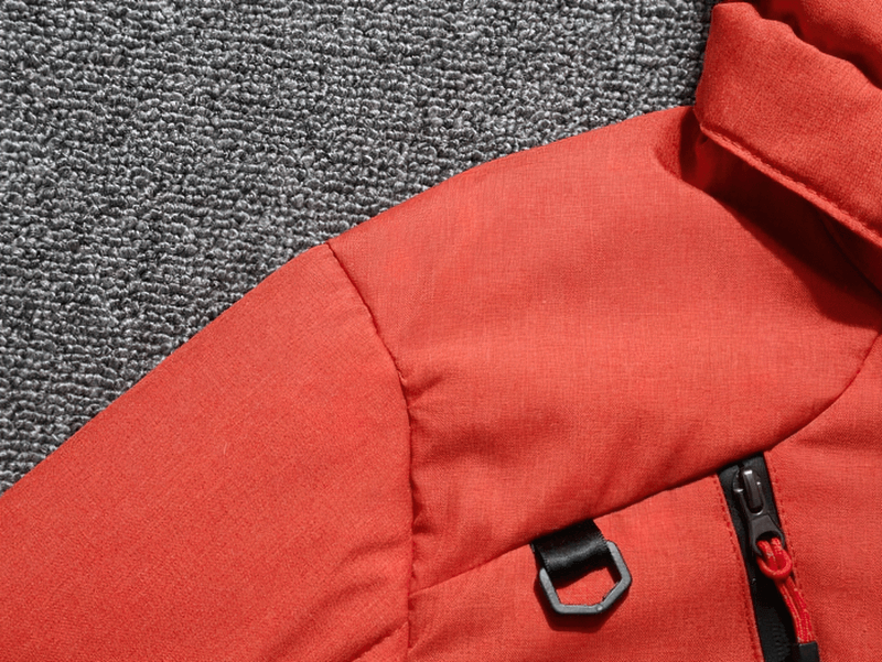 Close-up of a red ski suit jacket, featuring a durable fabric and zipper on a gray textured background, perfect for outdoor sports.
